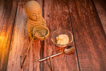 Buddah in warm light with coconut oil, tongue scraper and spoon. Ayuveda health with oil pulling.