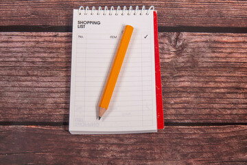 Shopping list in a blank notepad and a gleben pencil on a table ready to write down the wishes and purchases.