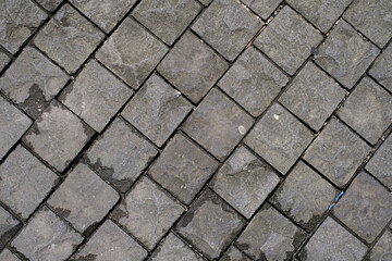 Black basalt paving which is wet because of the rain but has started to dry. Texture and material.
