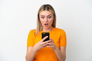 Young caucasian woman isolated on white background looking at the camera while using the mobile with surprised expression
