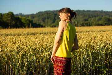 Frau mit gelben Shirt am Rand von Feldfrüchten an einem Weizenfeld, bei wolkenlosen Himmel und...