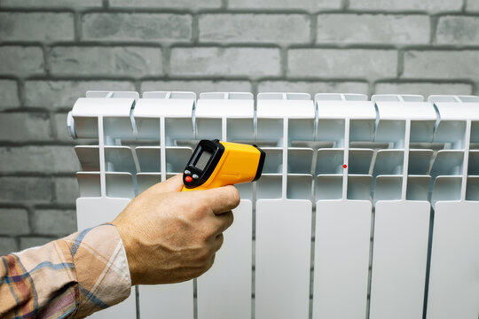 Technician measures the temperature of the heater radiator. Infrared thermometer in male hand. Heat leak detection.
