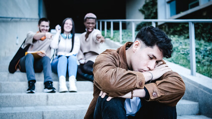 A group of students bulling an hispanic man sitting on the stairs outdoors