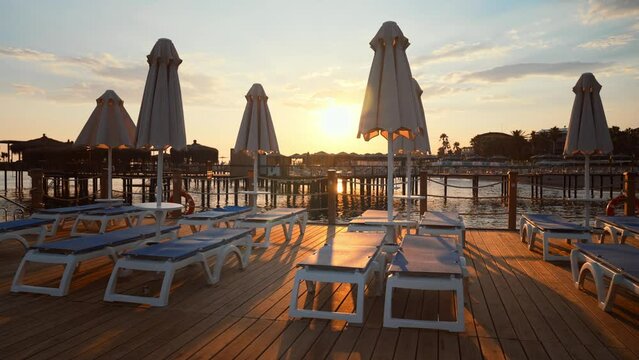 Sun umbrellas and beach chairs on wooden empty beach. Pier and sea in resort. Summer vacation in nature. Tourism and traveling. Rest and relaxation in recreation area to take sun rays and sunbathing.