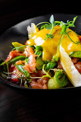 Salad with Boiled Eggs, Salmon, Tomatoes and cucumber in a bowl on black background