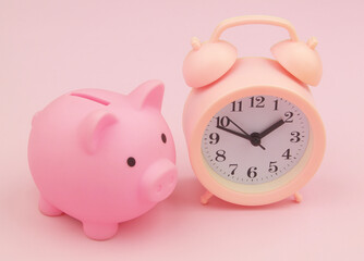 Pink piggy bank with alarm clock on pink background close up. Time for save money concept.