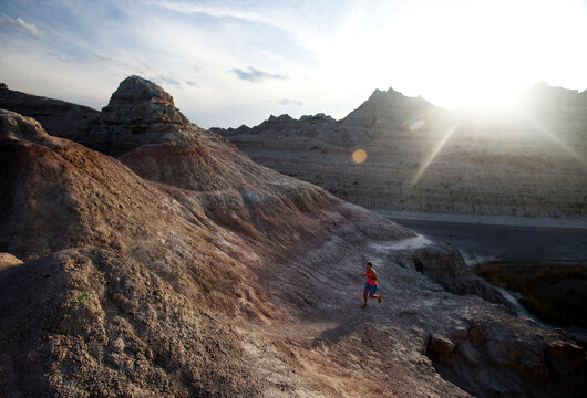 A young woman, wearing pink, runs along an unmarked trail in Badlands National Park at sunset.