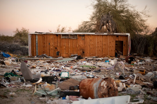 An abandoned trailer sits on its side with trash surrounding it.