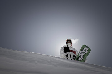 Portrait of backlit snowboarder standing with board on horizon.