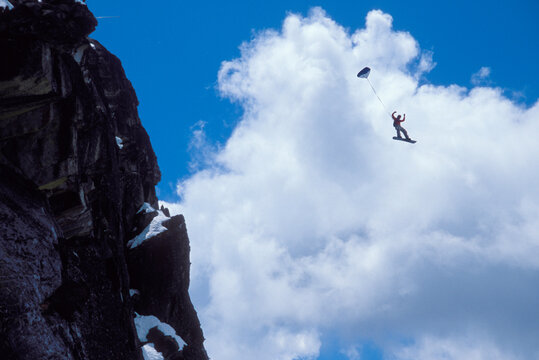 Snowboard-BASE jumper doing a backflip off a cliff near Lake Tahoe.