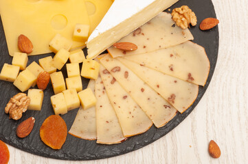 Different types of cheese on a black graphite board decorated with dried apricots and nuts