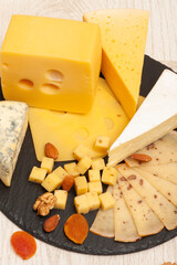 Different types of cheese on a black graphite board decorated with dried apricots and nuts