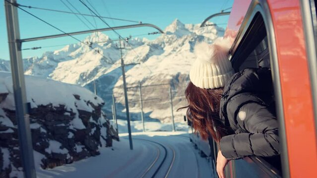 Happy woman traveler looks out from window traveling by train in beautiful winter mountains, Travel concept.
