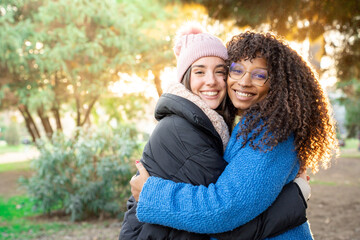 Portrait of smiling woman friends hugging each other on city street looking at camera