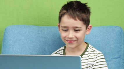 Kid face. A happy boy sitting on the bed in the nursery uses a laptop to play and go online. Kids use gadgets for games and distance learning. distantly work and training.