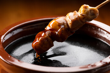 鶏のモモ肉の串焼きをタレ壺の中の焼き鳥のタレに漬ける