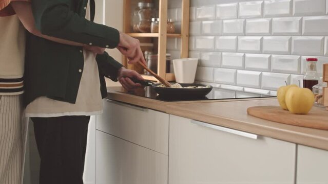 Cropped Slowmo Of Unrecognizable Gay Man Making Pasta In Frying Pan While His Boyfriend Hugging Him Tenderly From Behind Standing Together In Cozy Kitchen