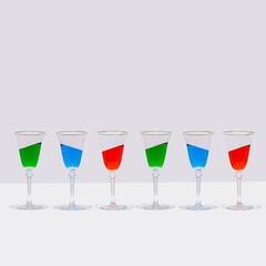 Six colorful cocktail glasses stand straight with the drink in them at an inclined angle. Surreal drinking culture, summer party or celebration composition.