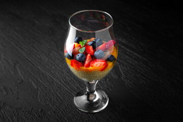 Fruit salad with chia, a healthy dessert in a glasson a dark textured background. Restaurant menu Isolated on black