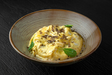 Polenta with mushroom julienne and truffle in a ceramic plate on a dark textured background. Restaurant menu Isolated on black