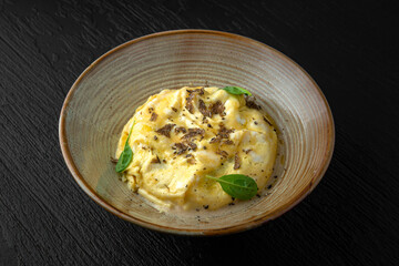 Polenta with mushroom julienne and truffle in a ceramic plate on a dark textured background. Restaurant menu Isolated on black