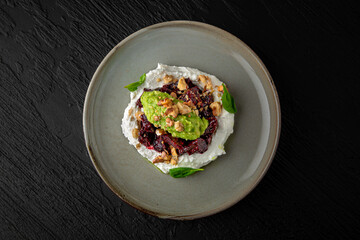 Dried beets with young cheese and guacamole in a ceramic plate on a dark textured background. Restaurant menu Isolated on black