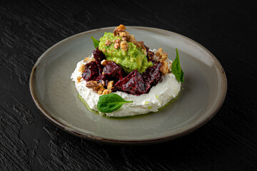 Dried beets with young cheese and guacamole in a ceramic plate on a dark textured background. Restaurant menu Isolated on black