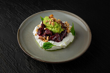Dried beets with young cheese and guacamole in a ceramic plate on a dark textured background. Restaurant menu Isolated on black