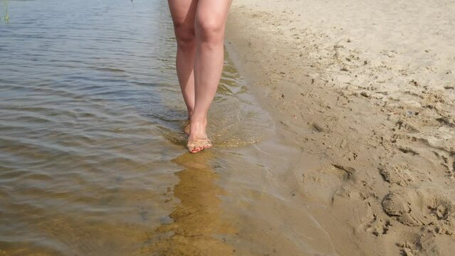 View of a woman's legs in the water near the beach. A woman walks on water. Waves of water in the river. Slow motion leg movement