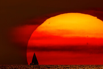 Silhouette of a sailing boat in sunset sunrise time and ocean horizon.