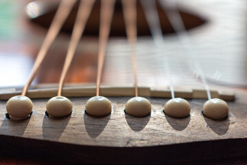 Acoustic guitar bridge with one pins and strings close up with selective shallow focus and blur.