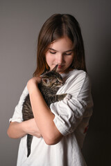 Teengirl holding a baby cat on gray background. Kitten sits on the female shoulder. Vertical photo. Side view