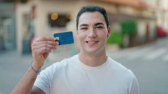 Young hispanic man smiling confident holding credit card at street
