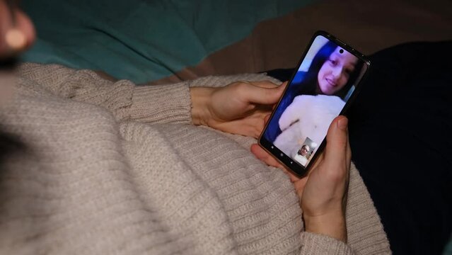 Young man sitting on sofa holding smartphone communicating with girl friend that show gim plush toy on mobile screen, making video call using cell phone mobile social media dating app
