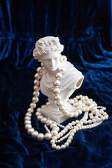sculpture of apollo surrounded by pearl beads on dark blue velvet. copy space. top view