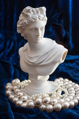 sculpture of apollo surrounded by pearl beads on dark blue velvet. close up. 