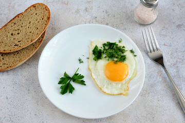 fried egg with yellow yolk isolated on white plate with slices of bread and fork, close-up