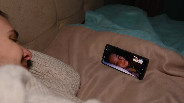 Young man lie on sofa holding smartphone communicating with girl friend that show gim plush toy on mobile screen, making video call using cell phone mobile social media dating app