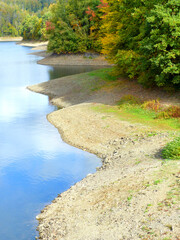 A beautiful place at a lake, reflecting the blue sky along some trees. A nature scenery of colorful woods in national park in late summer. 