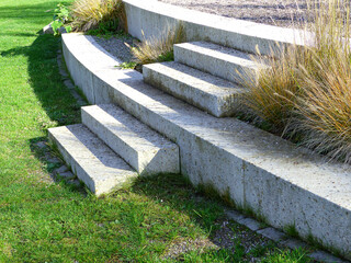 A few steps with some decorative grass tufts, leading up on a plateau, in a public park on a sunny day.