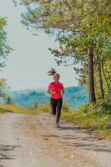 Young happy woman enjoying in a healthy lifestyle while jogging on a country road through the beautiful sunny forest, exercise and fitness concept
