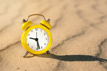 Yellow alarm clock on the sand in the desert on a hot sunny day with a dark shadow close up