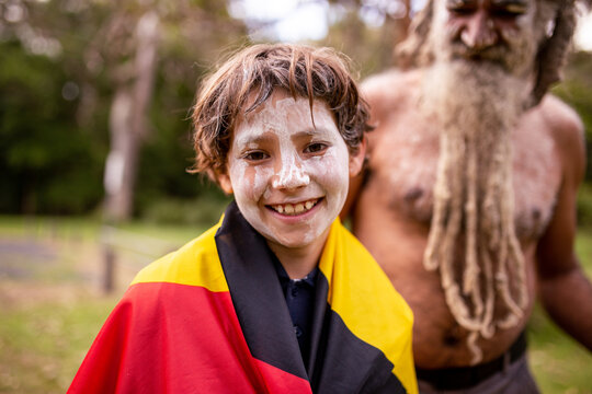 Young Aboriginal boy wearing the Aboriginal flag around his shoulders and smiling at the camera