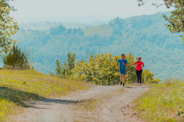 Obraz premium Couple enjoying in a healthy lifestyle while jogging on a country road through the beautiful sunny forest, exercise and fitness concept