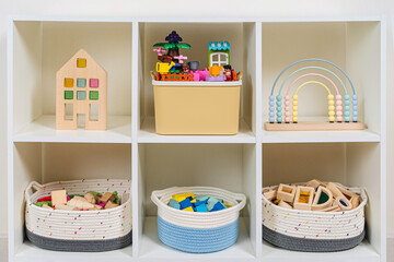 White shelving with rainbow wooden toys and constructor pieces in storage baskets and boxes....