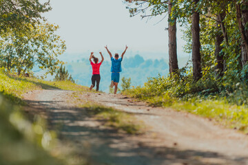 Obraz premium Couple enjoying in a healthy lifestyle while jogging on a country road through the beautiful sunny forest, exercise and fitness concept