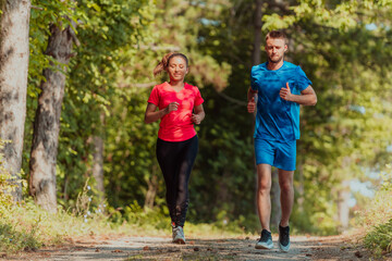 Fototapeta premium Couple enjoying in a healthy lifestyle while jogging on a country road through the beautiful sunny forest, exercise and fitness concept