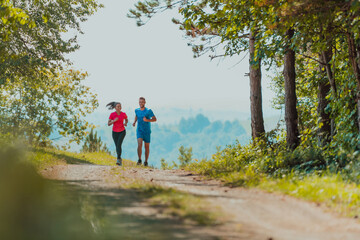 Obraz premium Couple enjoying in a healthy lifestyle while jogging on a country road through the beautiful sunny forest, exercise and fitness concept