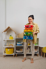 Young woman is holding storage boxes toys. Mom sorted by colors children's toys in transparent...