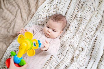 a small newborn baby girl is playing with an educational bright yellow rattle toy at home in the bedroom of the children's room on the bed. Close-up portrait.